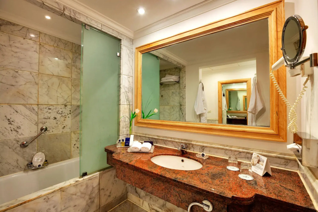 Savoy Sharm El Sheikh hotel: Marble-clad bathroom with a long vanity, basin, large framed mirror, and visible toiletries.