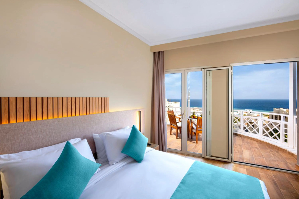 AJIRA Resort Sahl Hasheesh: A bright bedroom opens onto a furnished balcony with views of the sea.