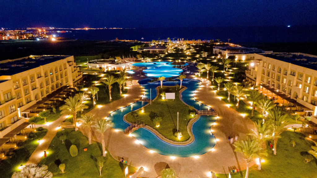 Mövenpick Waterpark Resort & Spa Soma Bay: Aerial night view of illuminated resort pools winding through palm-lined grounds between resort buildings.