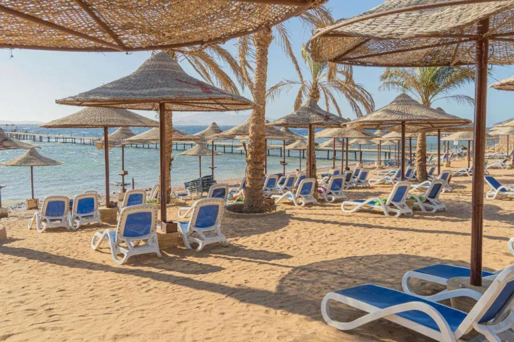 Tamra Beach Resort: Blue sun loungers and shaded seating line a sunny sandy beach beside the sea.