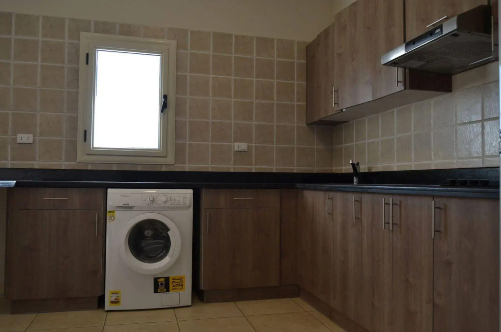 Rivoli Suites: A fitted kitchenette with a front-loading washing machine, tiled backsplash, and overhead range hood.