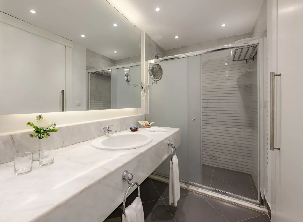 Desert Rose Resort: Bright bathroom with a marble vanity, large mirror, and glass-enclosed walk-in shower.