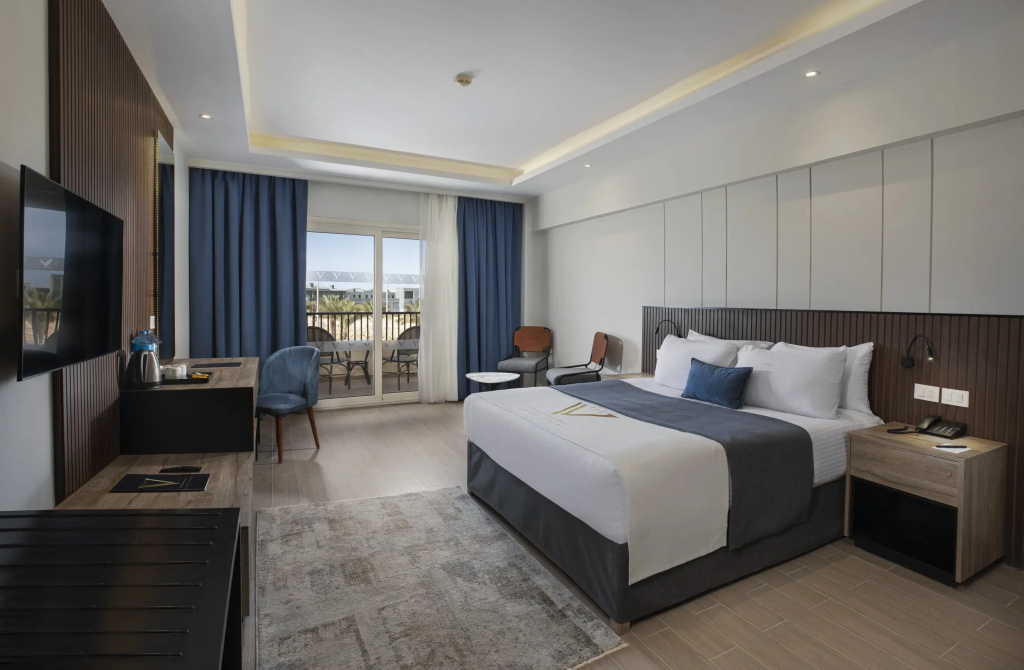 V Luxury Resort Sahl Hasheesh: Modern guest room with a king bed, a seating area, and glass doors opening to a balcony.