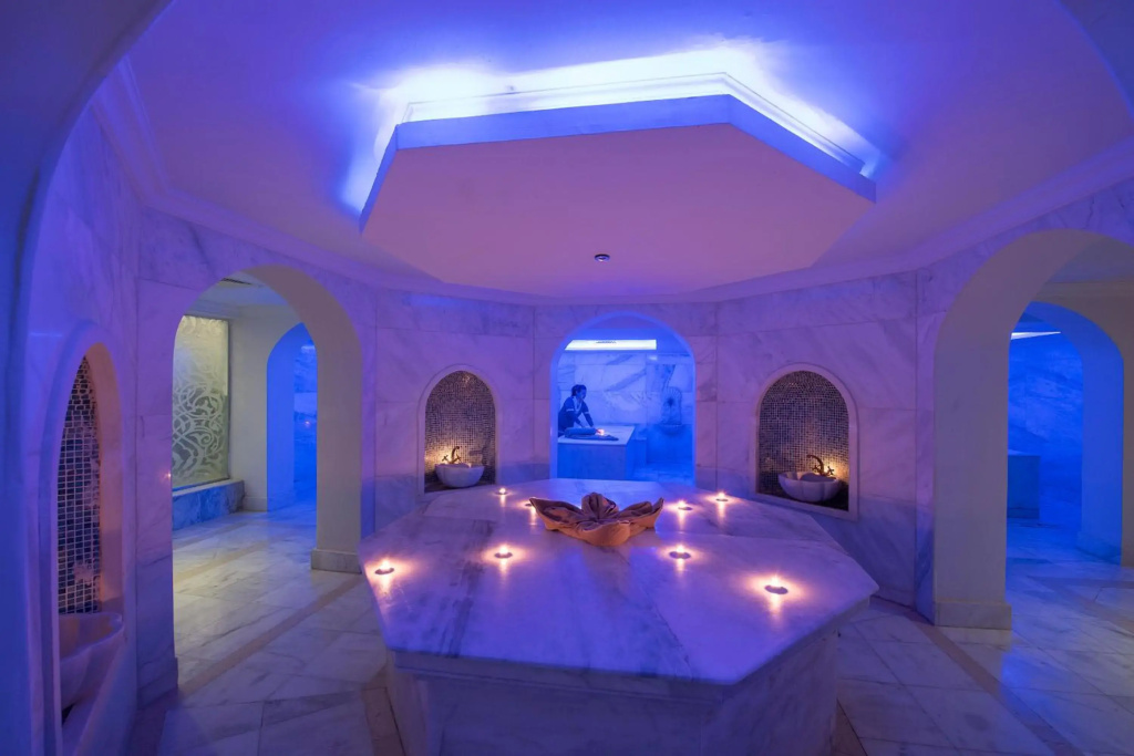 Baron Palace Sahl Hasheesh Resort: A marble spa room features a central treatment platform, arched alcoves, and atmospheric blue lighting.