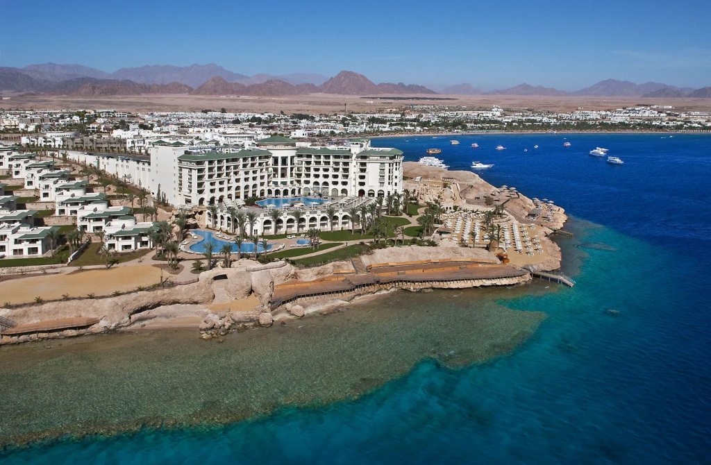 صورة: Stella Di Mare Beach Hotel & Spa Resort: A large beachfront resort with outdoor pools, rows of sun loungers, and clear blue water along a rocky shoreline.