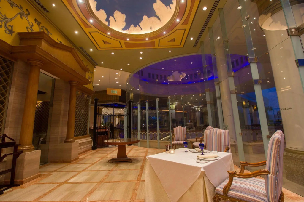Royal Monte Carlo Sharm El Sheikh - Adults only: An elegant restaurant dining area with a formally set table, striped upholstered chairs, and a decorative high ceiling.