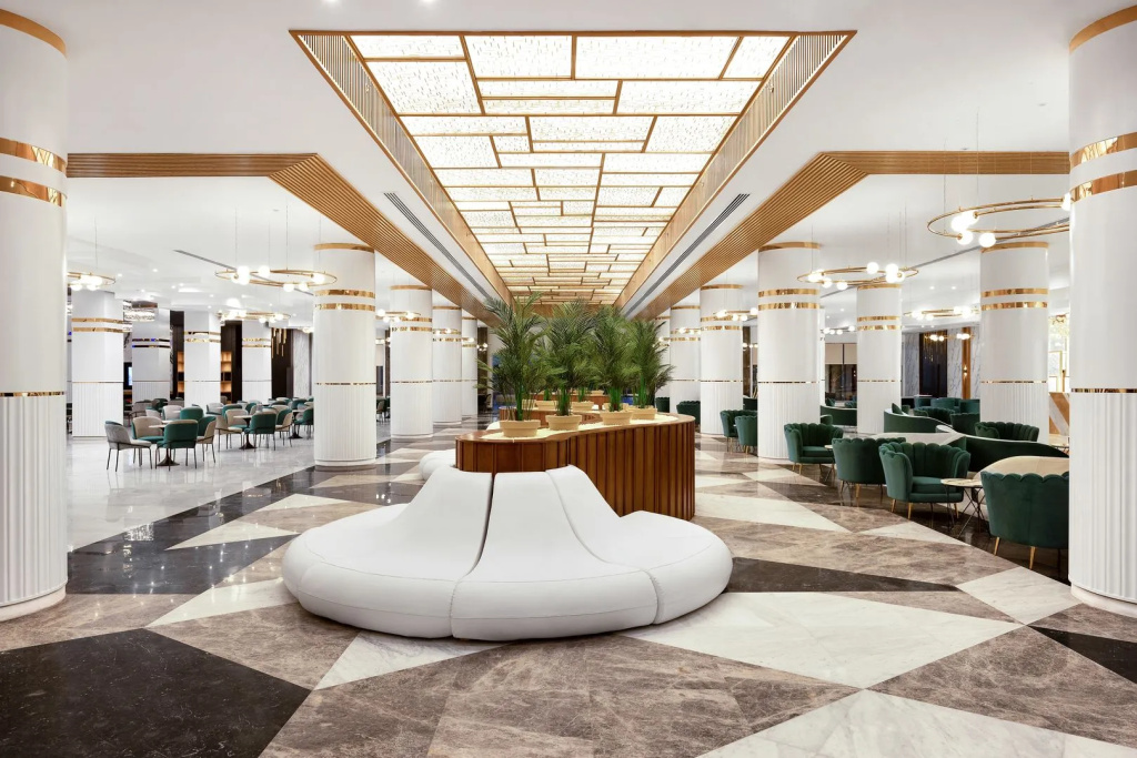 V Luxury Resort Sahl Hasheesh: A bright, spacious lobby lounge with plush seating, marble-patterned floors, and a striking wood-accented ceiling.