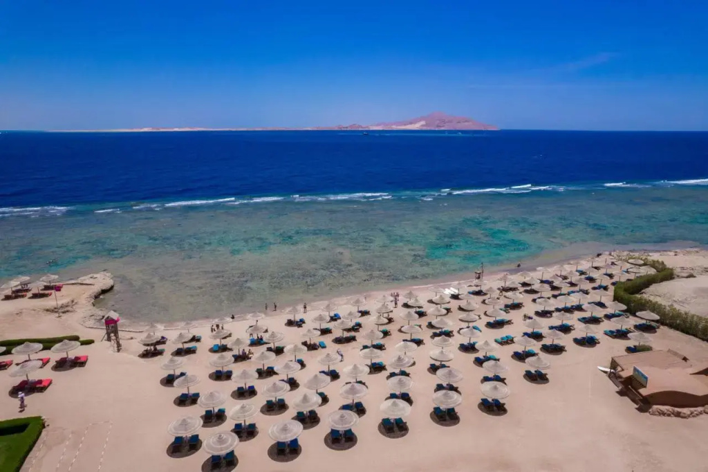 Charmillion Gardens Aquapark: Rows of sun loungers and parasols line a sandy beach beside clear blue water.