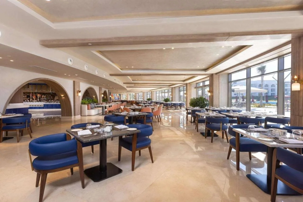 Club Prive By Rixos Sharm El Sheikh: A bright, spacious restaurant with neatly set tables, blue upholstered seating, and a bar counter.