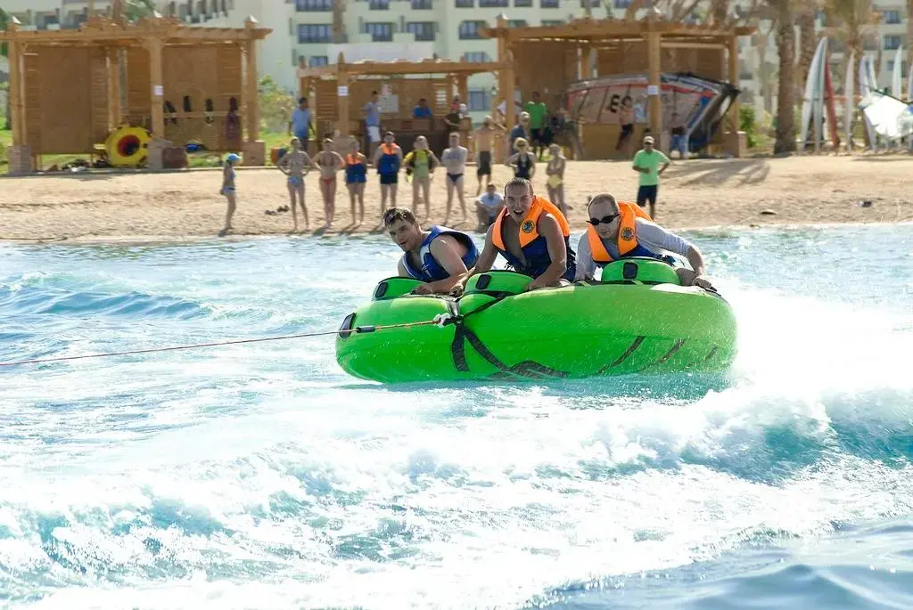 Steigenberger Aqua Magic Hotel: Guests ride a green inflatable raft through choppy water beside a sandy resort shoreline.