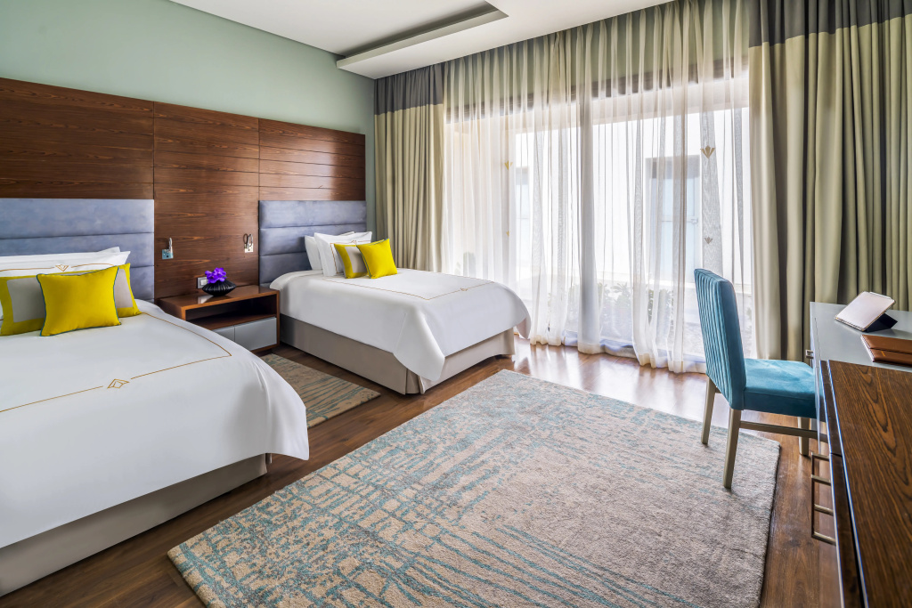 Rixos Premium Magawish Suites and Villas: Bright twin bedroom with two beds, a desk, and a large curtained window.