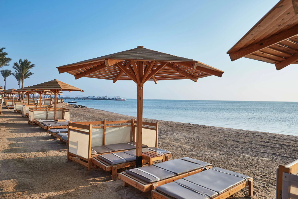 Steigenberger Aqua Magic Hotel: Relax on cushioned loungers beneath wooden shades along the sandy beach.