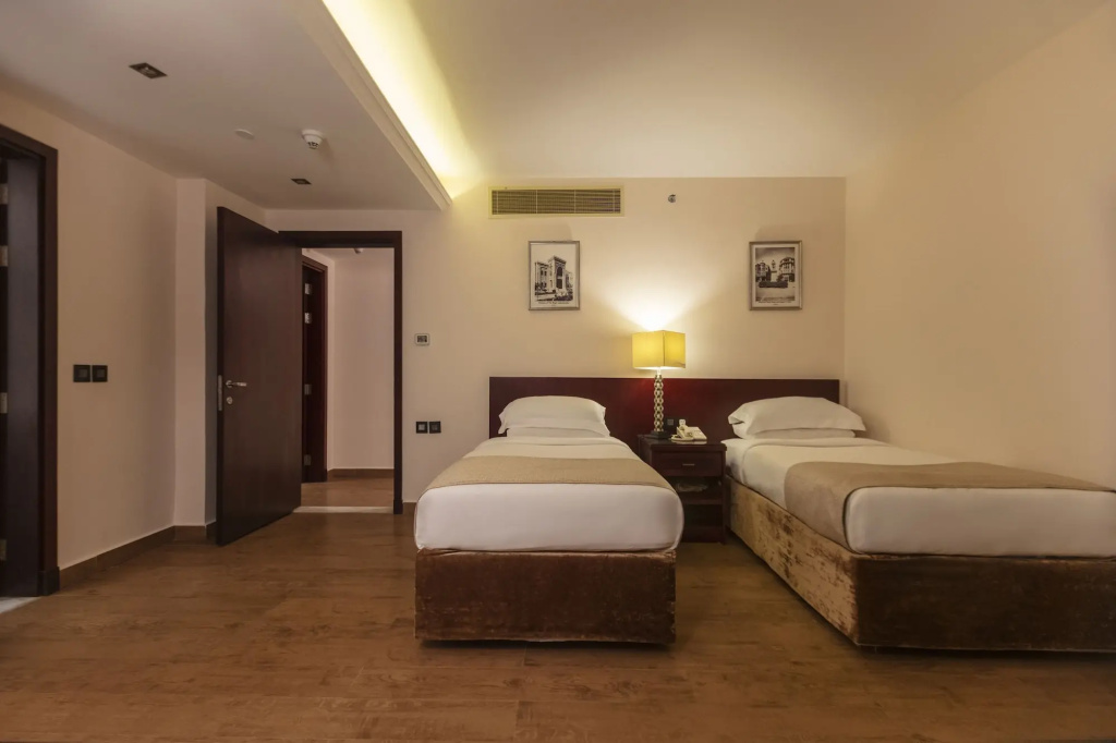 Royal Savoy Sharm El Sheikh: A warm-toned twin bedroom with two neatly made beds, a shared bedside table, and soft ambient lighting.