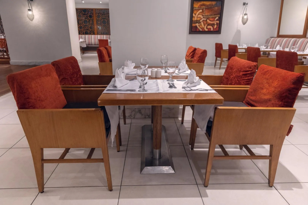 Old Palace Sahl Hasheseh: A warmly furnished dining room with set tables, wooden chairs, and rust-colored upholstered seats.