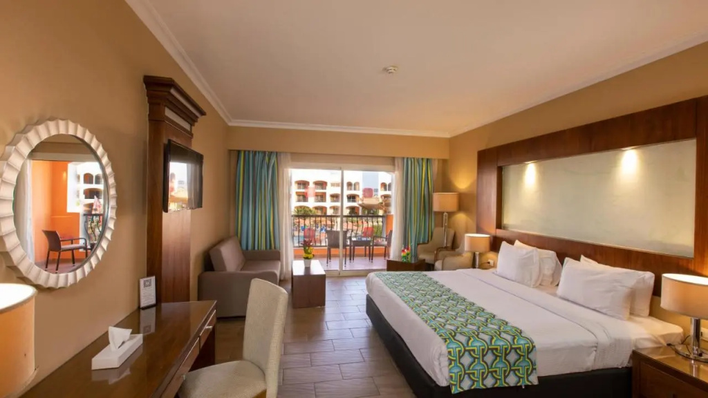 Naama Waves Hotel: Spacious bedroom with a king bed, seating area, wall-mounted TV, and balcony access.