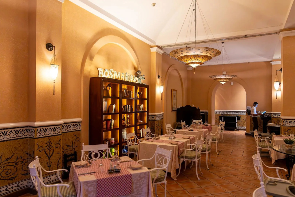Savoy Sharm El Sheikh hotel: A warmly lit dining room with set tables, white chairs, and decorative chandeliers.