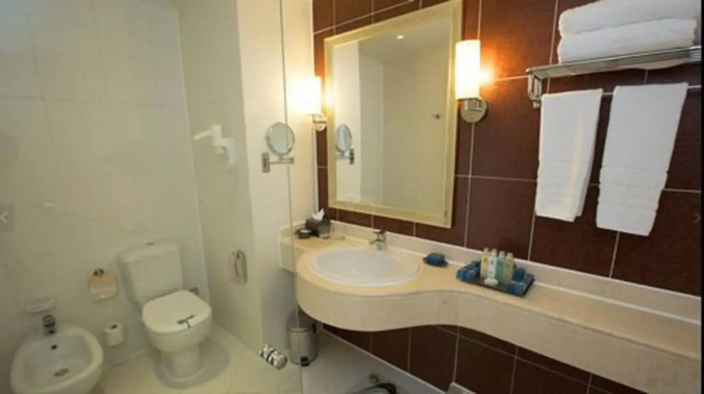 Baron Palace Sahl Hasheesh Resort: A bathroom with a curved vanity, large mirror, toilet, bidet, and fresh towels.