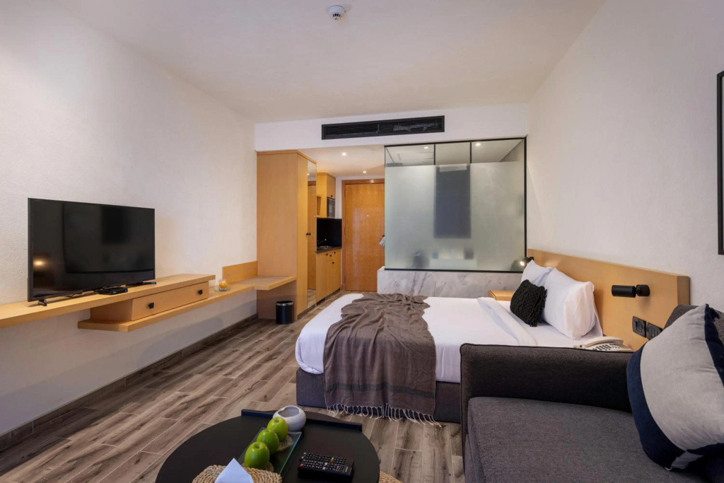 Creek Hotel and Residences El Gouna: A modern guest room with a double bed, seating area, television, and warm wood finishes.