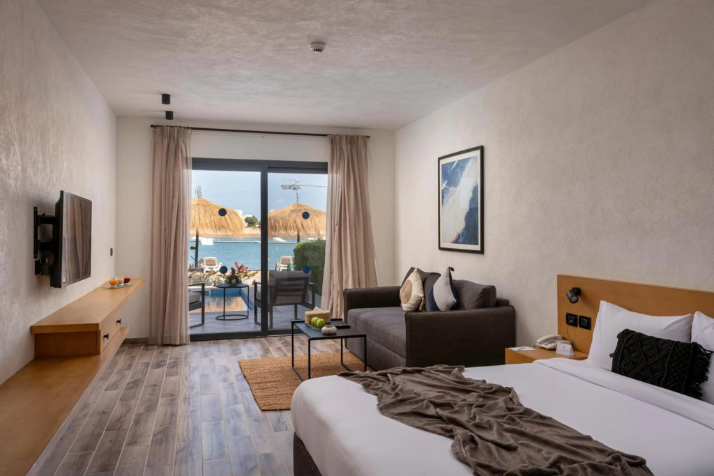 Creek Hotel and Residences El Gouna: A bright guest room with a bed, sofa seating, and a furnished terrace overlooking the water.