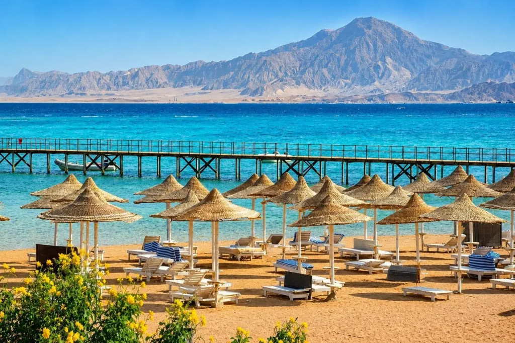Regency Plaza Aqua Park & SPA: Relax on a sandy beach beneath thatched umbrellas, with clear turquoise water and mountain views.