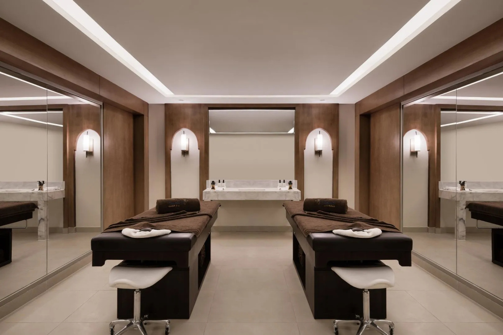 Xanadu Makadi Bay - High Class All Inclusive: A serene spa treatment room with two massage beds, warm wood finishes, and mirrored walls.