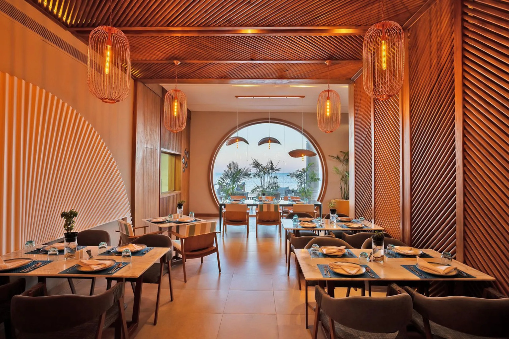Rixos Premium Magawish Suites and Villas: Warmly lit restaurant dining room with neatly set tables and a sea view.