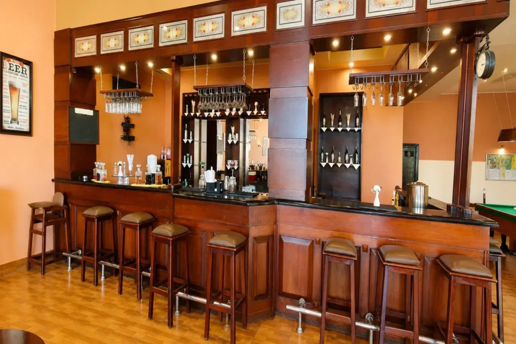 Royal Regency Club - Ultra All Inclusive: A warm-toned bar with a long counter, bar stools, and bottle displays.