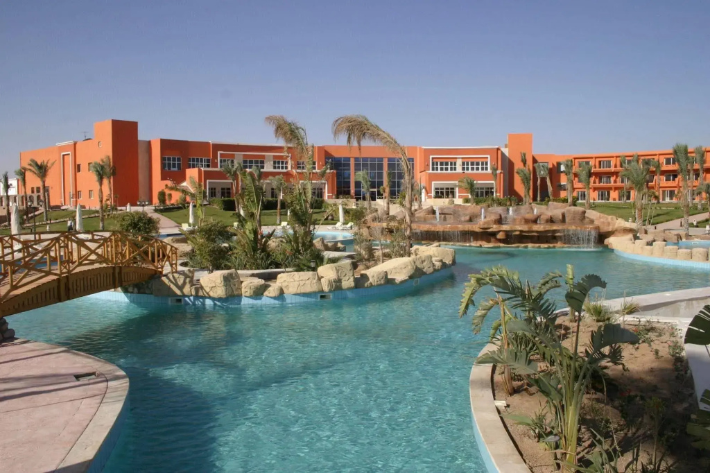 صورة: Amwaj Oyoun Resort & Casino Resort: A turquoise outdoor pool winds through landscaped grounds with palm trees and rock features, in front of the resort.