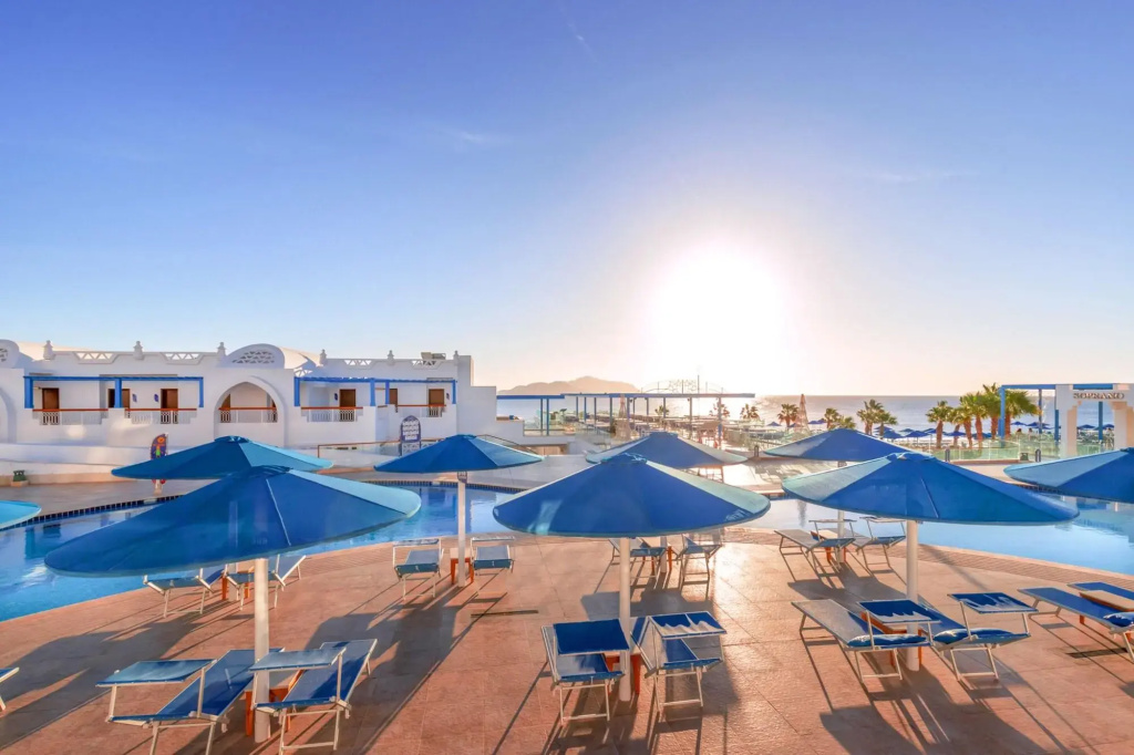 Pickalbatros Palace Sharm & Aqua Park: An outdoor pool deck with blue sun loungers and shade umbrellas, overlooking the sea.