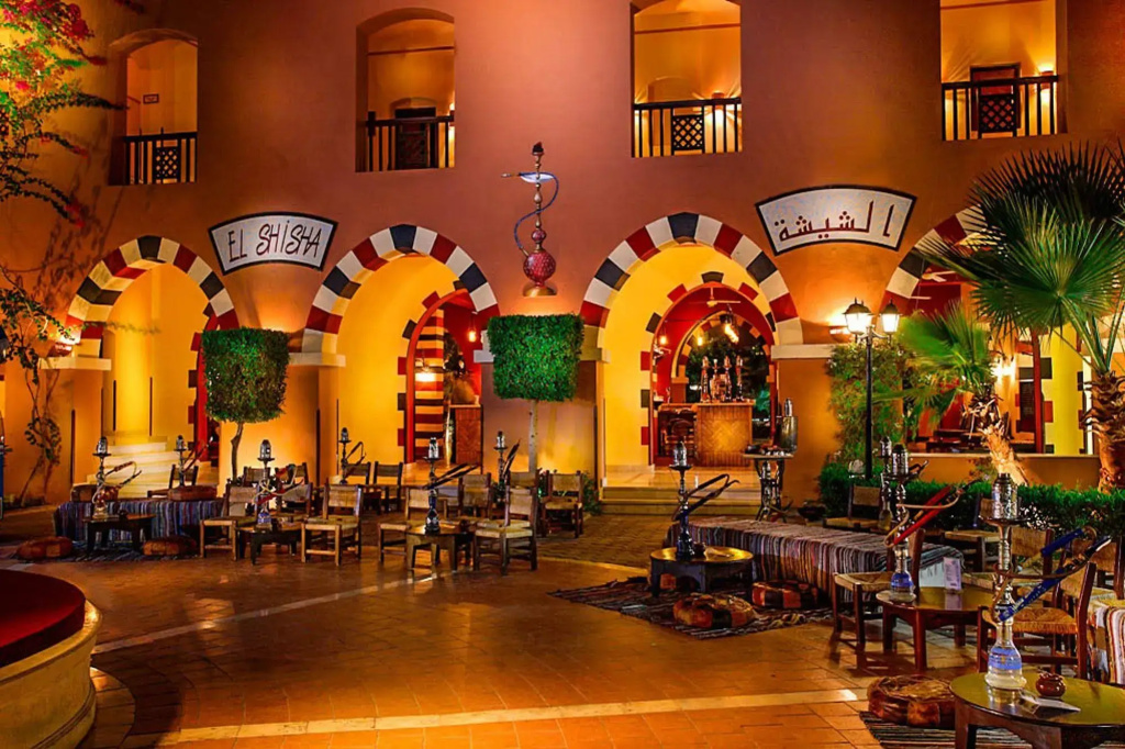 JAZ Makadi Saraya Resort: A warmly lit shisha lounge with hookah tables, cushioned seating, and colorful arched surroundings.