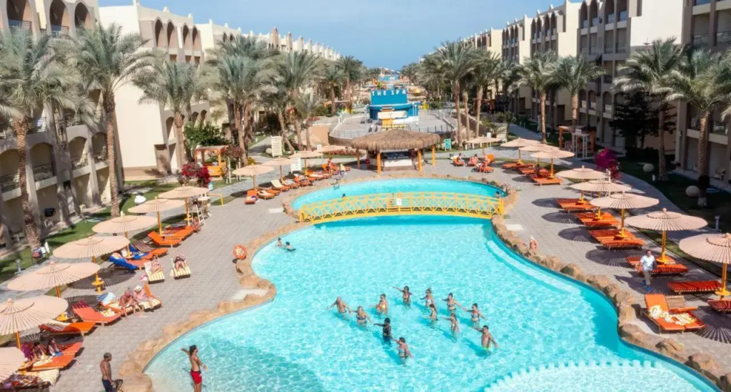 El Karma Aqua Beach Resort: A large outdoor pool is surrounded by sun loungers and parasols in a palm-lined resort courtyard.
