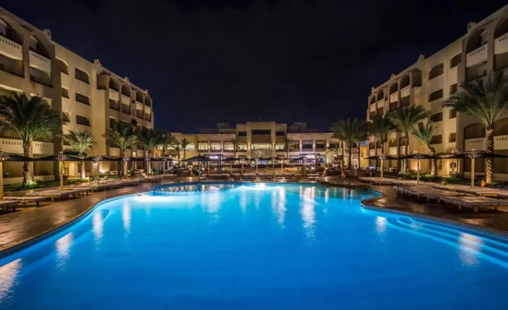 El Karma Aqua Beach Resort: A large illuminated outdoor pool sits in a palm-lined resort courtyard, surrounded by multi-story buildings.