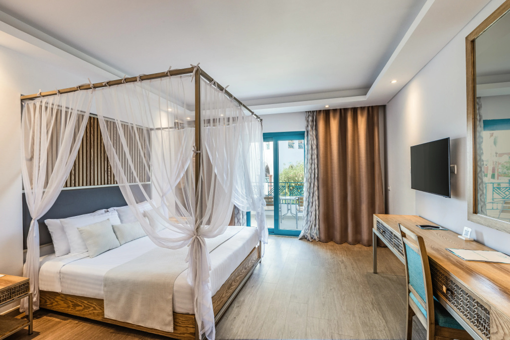 SUNRISE Garden Beach Resort: Bright guest bedroom with a canopy bed, wall-mounted TV, desk, and balcony access.