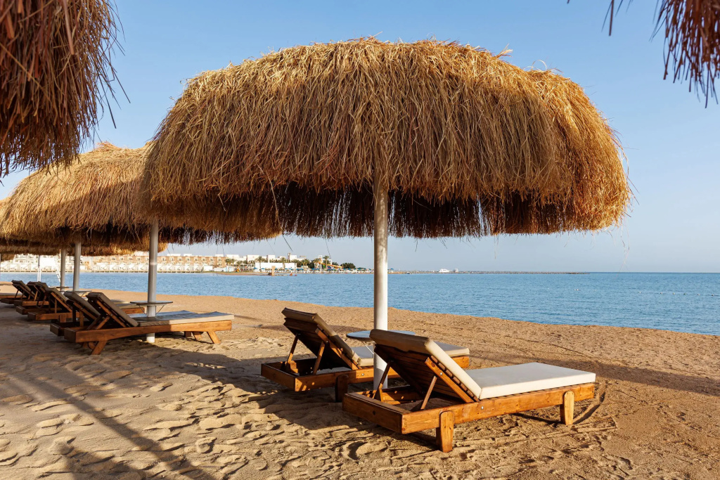 Solara Aqua Park Resort by SUNRISE: Wooden sun loungers sit beneath thatched parasols on a sandy beach overlooking the sea.