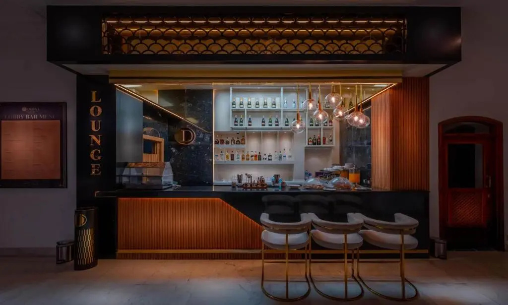 Domina Coral Bay Resort: A warmly lit lounge bar features a stocked bottle display and bar stools.