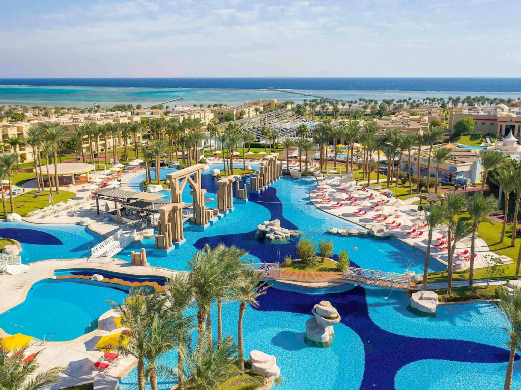 Rixos Premium Seagate: A sprawling turquoise pool with sun loungers and palm-lined grounds, with the sea visible beyond the resort.