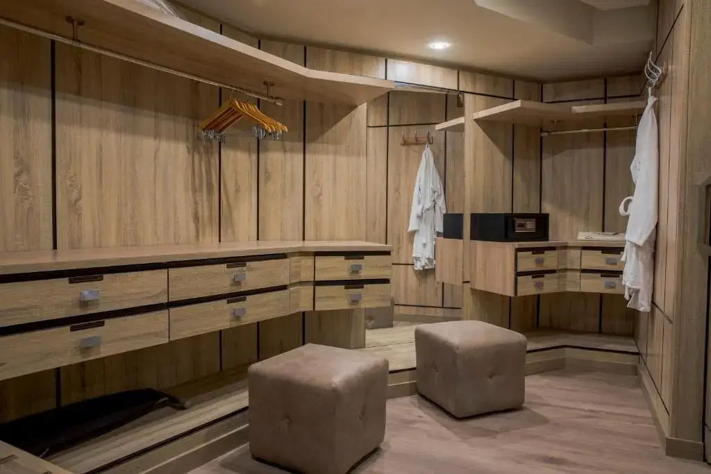 Pickalbatros Citadel Resort: A spacious wood-paneled dressing room with built-in drawers, hanging space, a safe, and two upholstered stools.