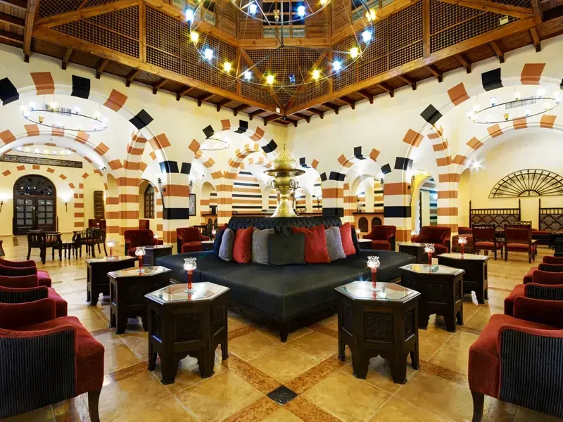 JAZ Makadi Oasis Resort: A spacious lobby lounge with sofas and armchairs arranged around low tables beneath a high, decorative ceiling.