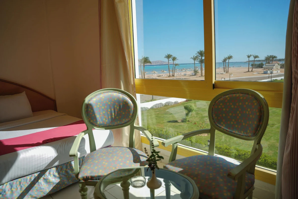 Sun Resort Aqua Park Sharm El-Sheikh: A bright bedroom with a bed, two upholstered chairs and a glass-top table overlooking the palm-lined beach and sea.